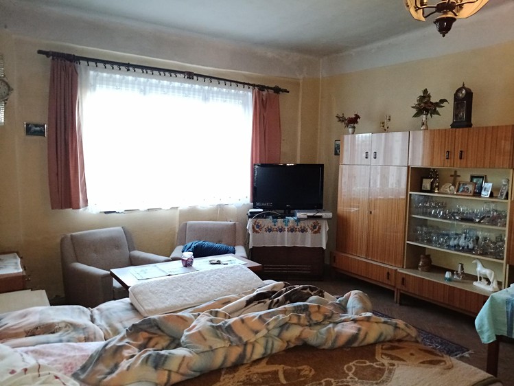 Obývací pokoj s nábytkovou stěnou, posezením a postelí v popředí.