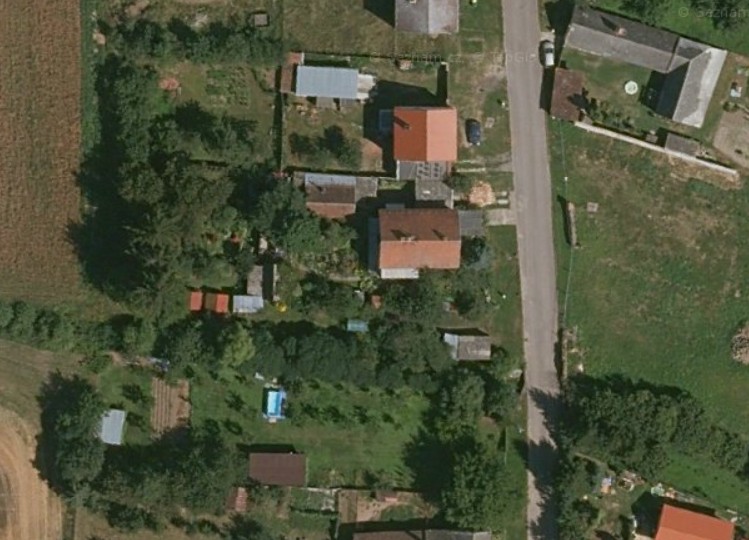 Letecký pohled na rodinný dům se zahradou, bazénem a hospodářskými budovami u silnice.