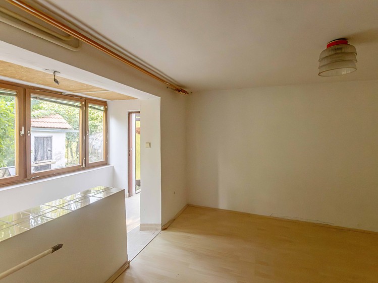 Světlý pokoj s dřevěnou podlahou, oknem do zahrady a průchodem na terasu.