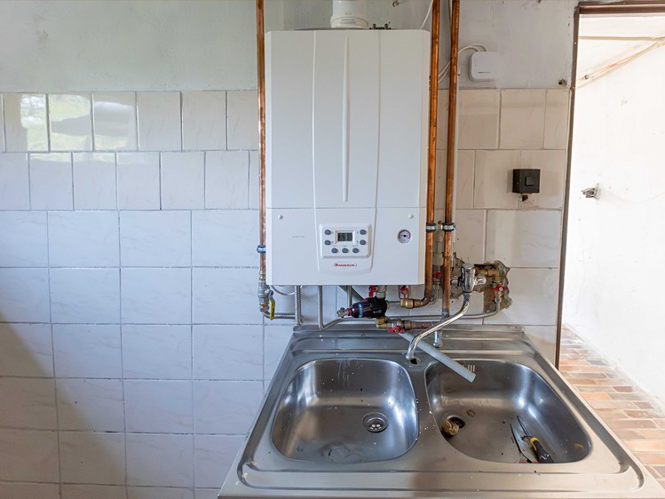 Plynový kotel nad nerezovým dřezem v místnosti s obklady.