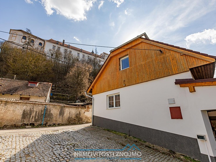 Dům s dřevěným štítem a dlážděným dvorem pod historickým zámkem.