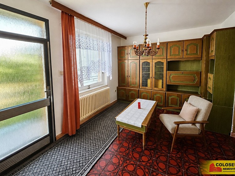 Interiér obývacího pokoje s retro nábytkem, křeslem, konferenčním stolkem a prosklenými dveřmi.