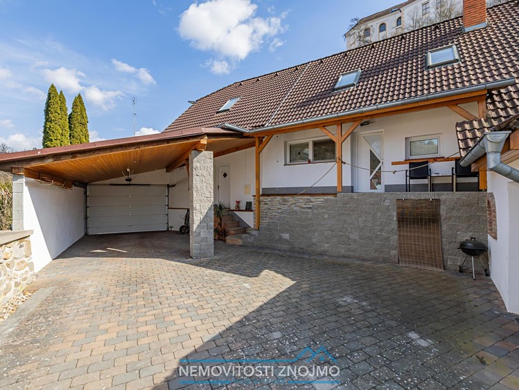 Dům s krytým parkovacím stáním, garáží a dlážděným dvorem.