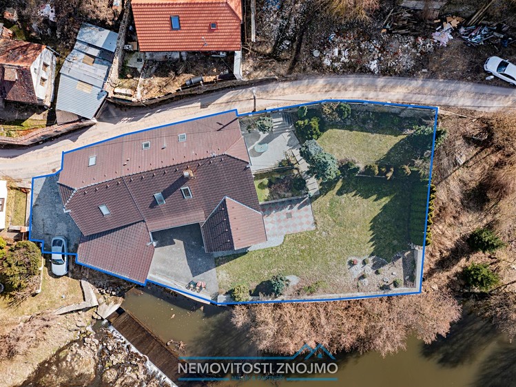 Letecký pohled na rodinný dům se zahradou u řeky a vyznačeným pozemkem.