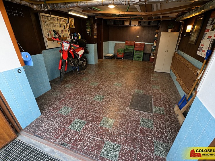 Garáž s motorkou, úložnými boxy, pracovním panelem na nářadí a dlažbou.