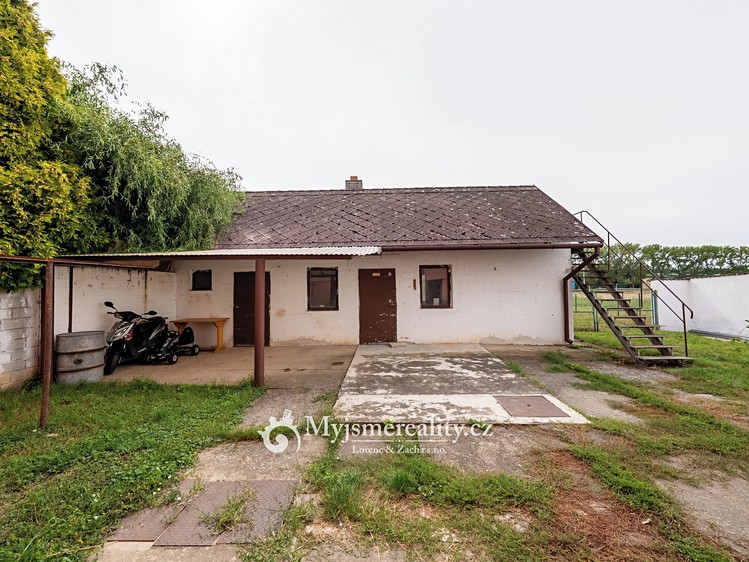 Přízemní dům s venkovním schodištěm, zastřešenou terasou a motorkou.