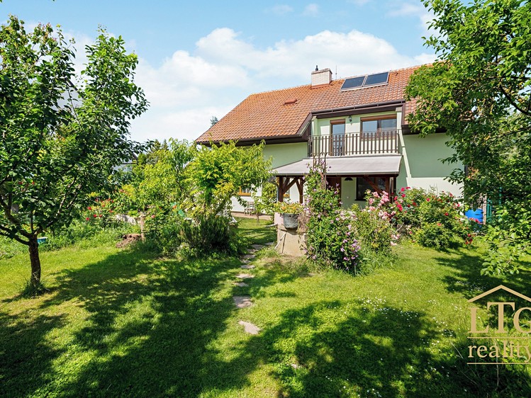 Zahrada s trávníkem a cestičkou před rodinným domem s terasou a balkonem.